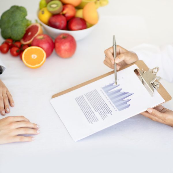Adult caucasian nutritionist doctor in white coat shows weight loss plan to young lady patient in clinic office interior. Proper nutrition, recommendation and advice by professional, health care